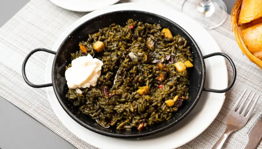 Arroz negro con sepia, un plato de mariscos oscuro y sabroso, servido en una paellera con una cucharada de alioli.