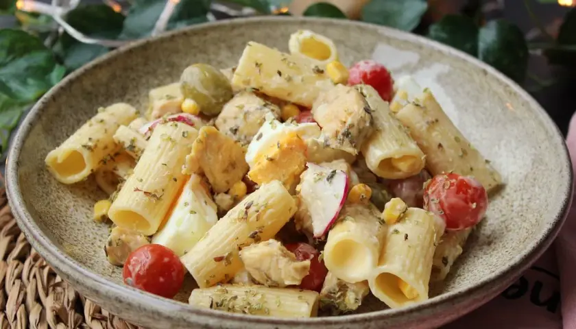Deliciosa ensalada de pasta con pollo, huevo duro, tomates cherry, aceitunas y maíz, aderezada con hierbas.