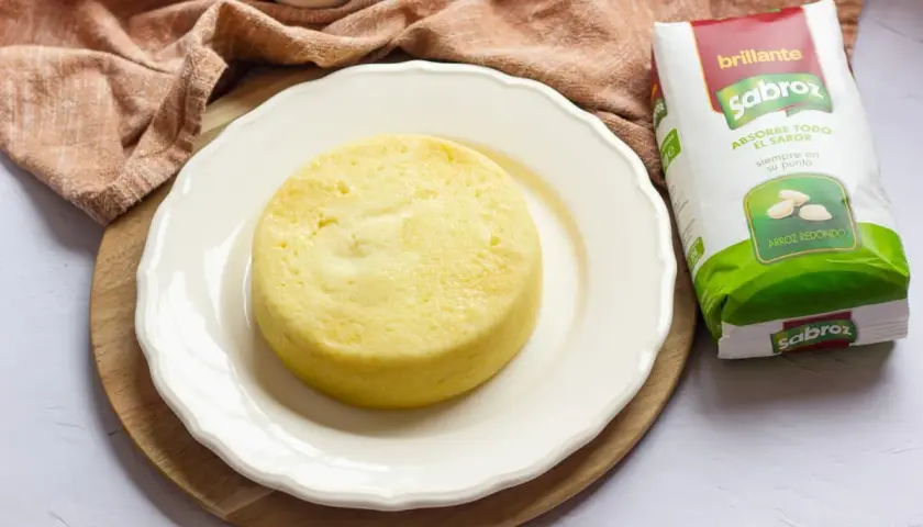 Pastel de arroz amarillo, esponjoso y redondo, servido en plato blanco junto a un paquete de arroz Sabroz.