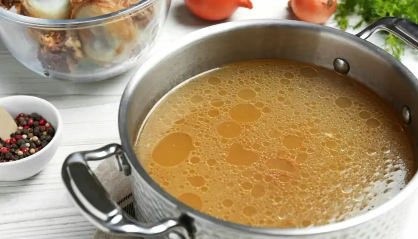 Olla con caldo de huesos burbujeante, junto a un bol con granos de pimienta y laurel, y otro con huesos.