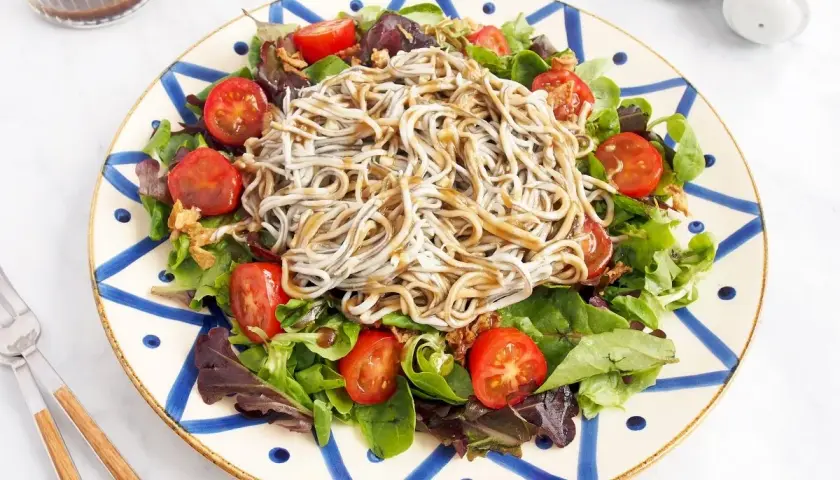 Deliciosa ensalada de gulas con tomates cherry y hojas verdes, servida en un plato decorado.