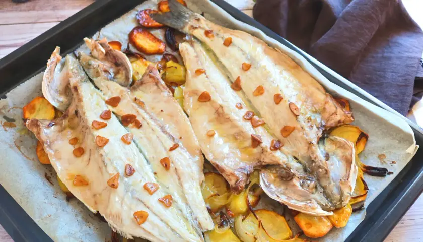 Lubina a la donostiarra recién horneada, con patatas y ajos dorados. Un plato delicioso y fácil de preparar.
