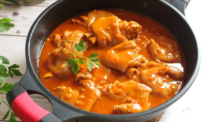 Manitas de cerdo en salsa roja, un plato tradicional español, servido en una sartén negra con perejil fresco.
