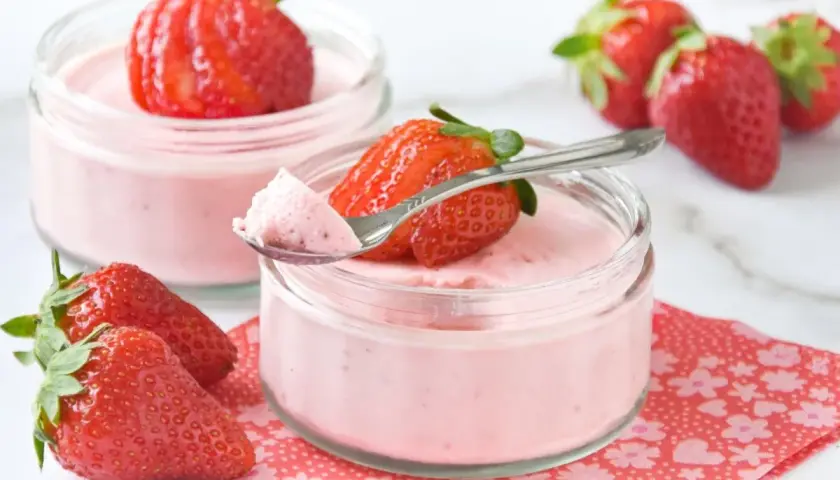 Delicioso mousse de fresa en vasitos, decorado con fresas frescas y una cucharita lista para probar.