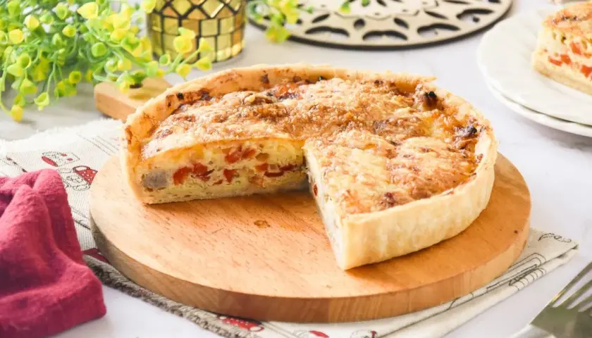 Un delicioso quiche de pollo, con trozos de pimiento rojo y queso gratinado, servido en una tabla de madera.