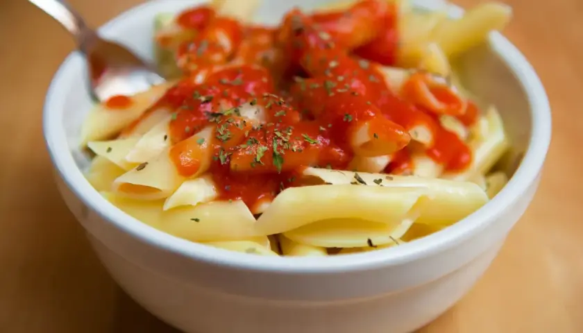 Un tazón de macarrones con tomate y hierbas, listo para disfrutar.