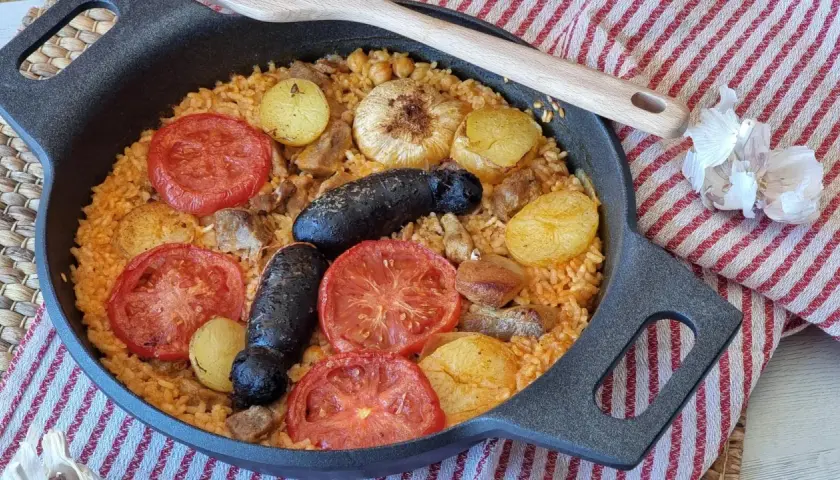 Delicioso arroz al horno con patatas, tomates, morcilla y garbanzos, listo para disfrutar.