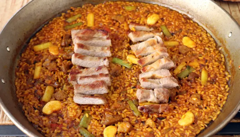Paella de secreto con trozos de cerdo a la parrilla, judías verdes y trozos de naranja.