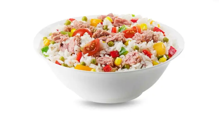 Un tazón blanco lleno de arroz con atún, guisantes, maíz, pimientos y tomates. Una comida fresca y colorida.
