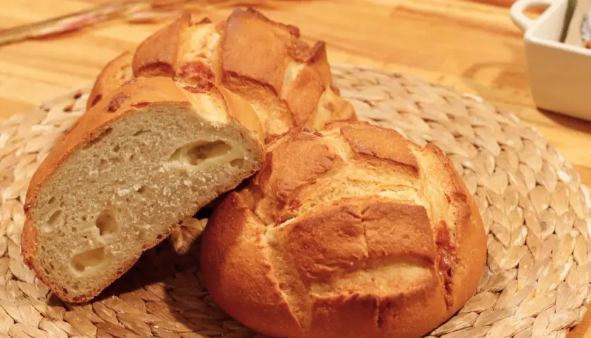 Pan de queso recién horneado, con una miga esponjosa y trozos de queso derretido visibles.
