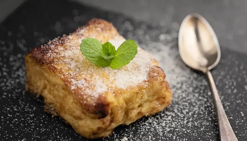 Torrijas con pan brioche, espolvoreadas con azúcar y decoradas con menta. Una cuchara plateada acompaña este delicioso postre.