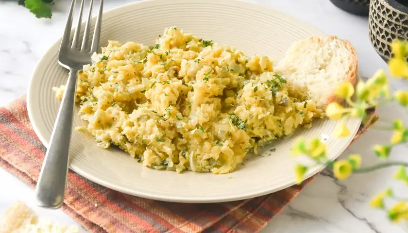 Un plato de bacalao a bras, desmenuzado y mezclado con patatas y perejil, servido con una rebanada de pan.