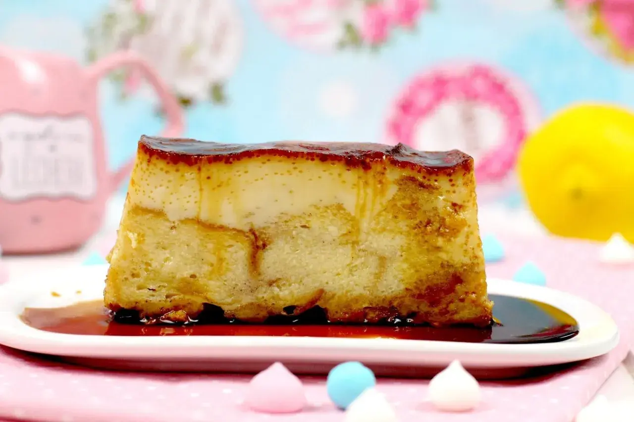 Un trozo de pan de calatrava con caramelo líquido sobre un plato blanco, adornado con merengues de colores y un limón al fondo.