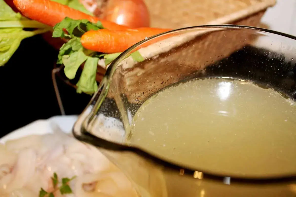 Un delicioso caldo de pescado casero, listo para usar en tu próxima receta. Zanahorias y apio en el fondo.