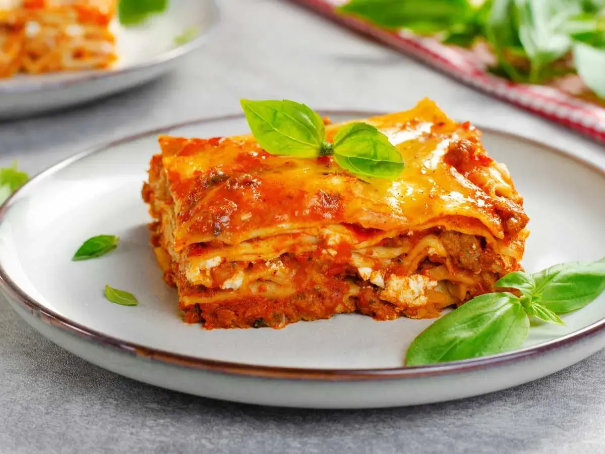 Una porción de lasaña de carne, con capas de pasta, salsa y queso, decorada con hojas de albahaca fresca.