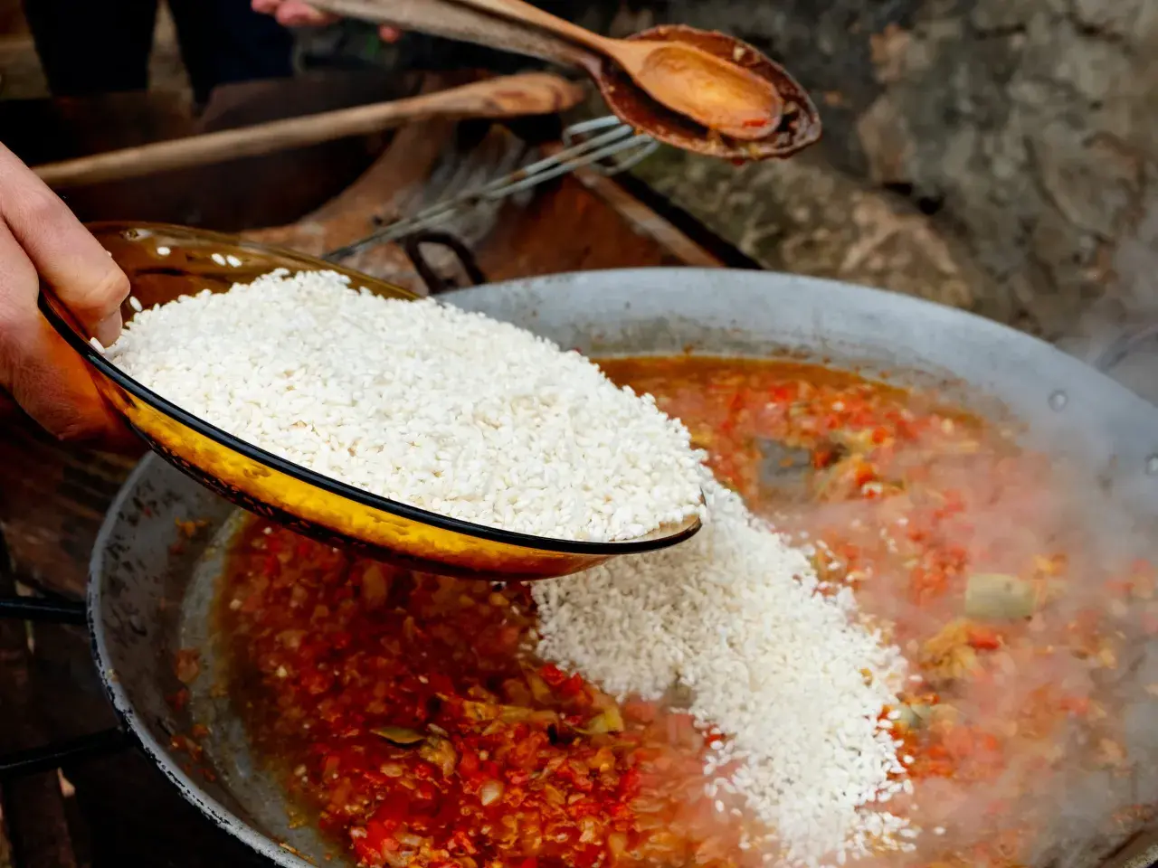 Se añade arroz a una paella de carne burbujeante con verduras rojas y verdes.