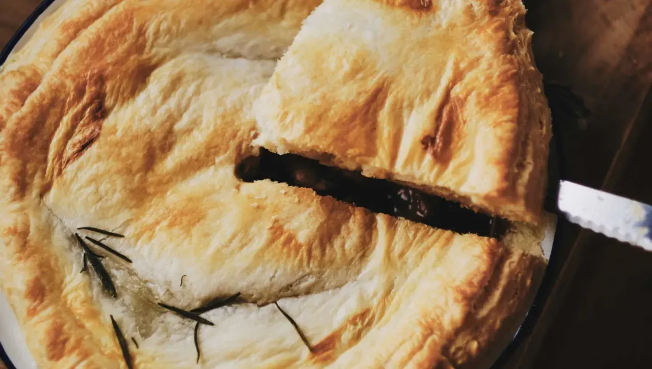 Un trozo de pastel con masa quebrada dorada, relleno oscuro y romero. Ideal para recetas con masa quebrada.