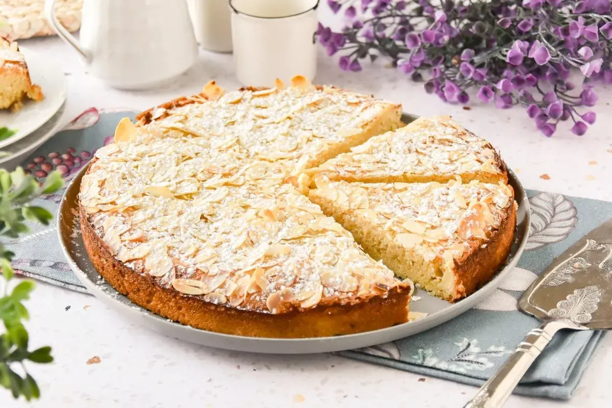 Tarta de almendras dorada, espolvoreada con azúcar glas y almendras laminadas, lista para servir.