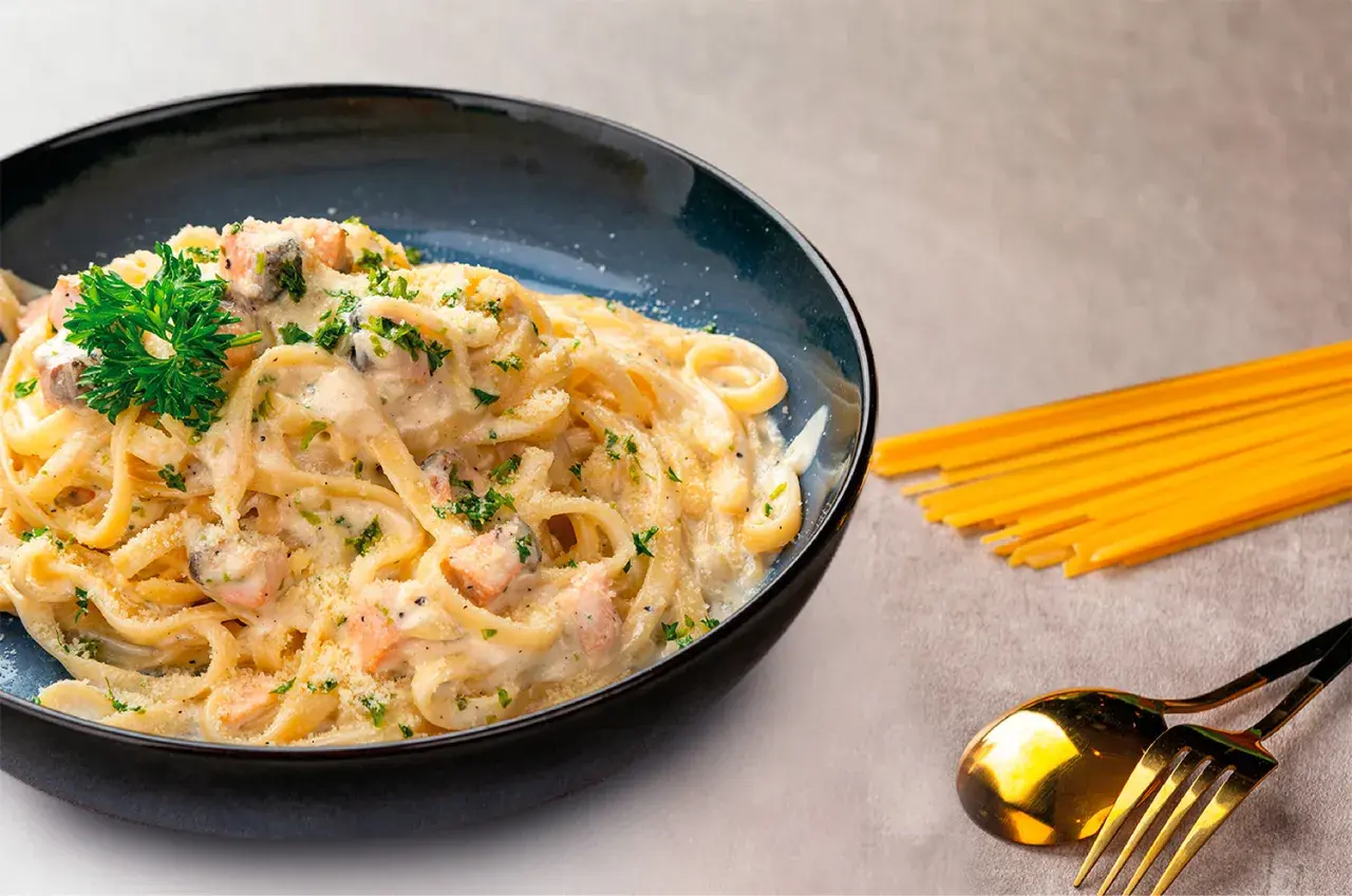 Deliciosa pasta con salmón cremoso, espolvoreada con perejil y queso rallado. Un plato perfecto para disfrutar.