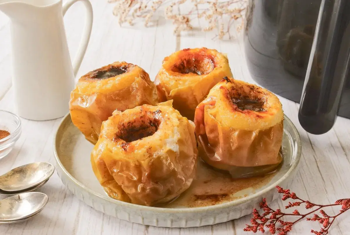 Cuatro manzanas asadas en freidora de aire, con el centro relleno de canela y azúcar, listas para disfrutar.