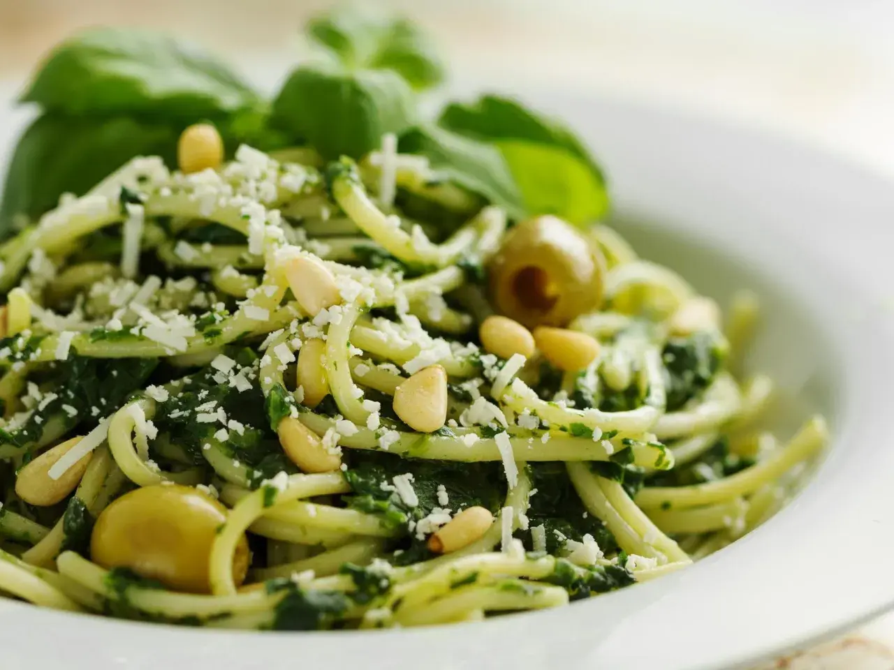 Deliciosa pasta al pesto, con piñones, aceitunas verdes y queso rallado, decorada con hojas de albahaca fresca.