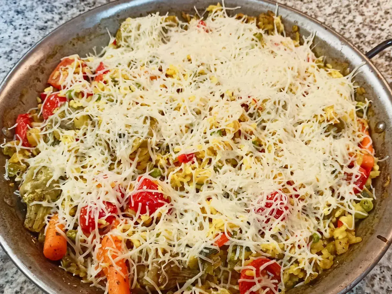 Arroz a la milanesa listo para hornear, cubierto con queso rallado y vegetales frescos como tomates, zanahorias y guisantes.
