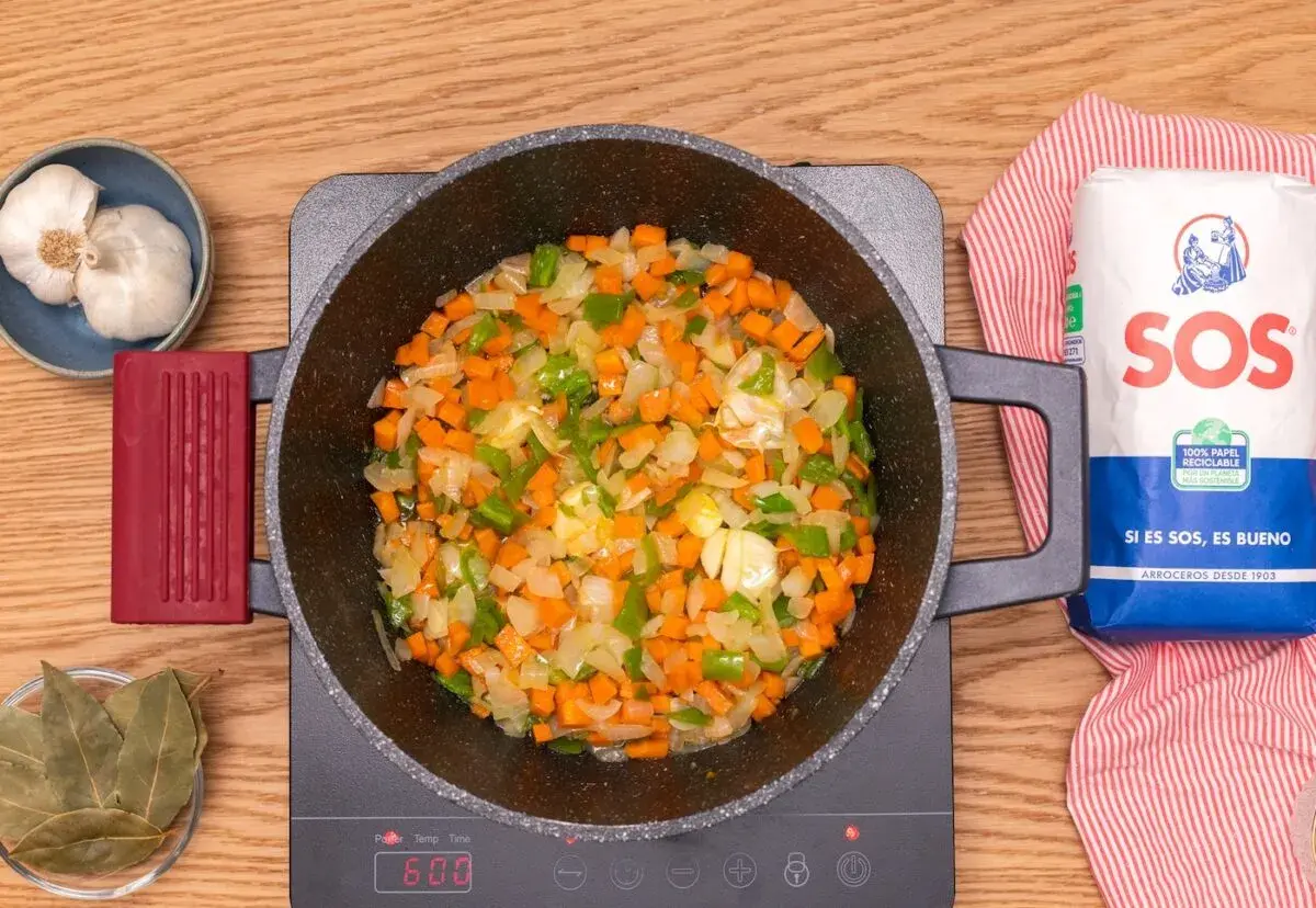 Verduras picadas (zanahoria, pimiento, cebolla) sofriéndose en una olla, listas para añadir lentejas con arroz.