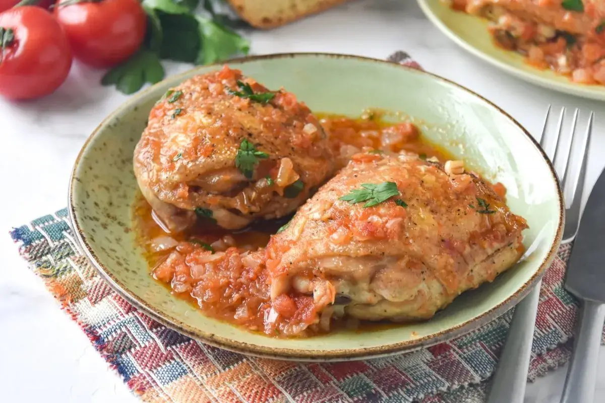 Dos jugosos contramuslos de pollo en salsa de tomate y cebolla, adornados con perejil fresco. Un plato casero y reconfortante.