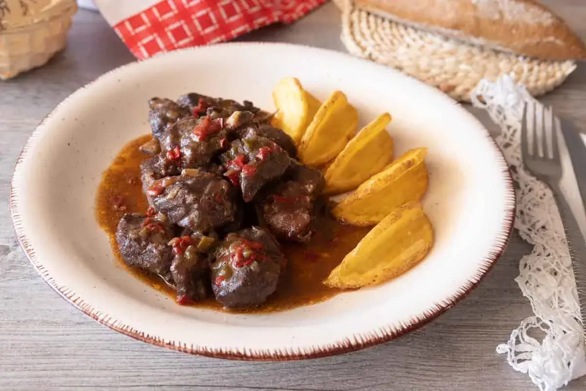 Sabrosa carne de cabra guisada con trozos de pimiento rojo y verde, servida con patatas gajo doradas.