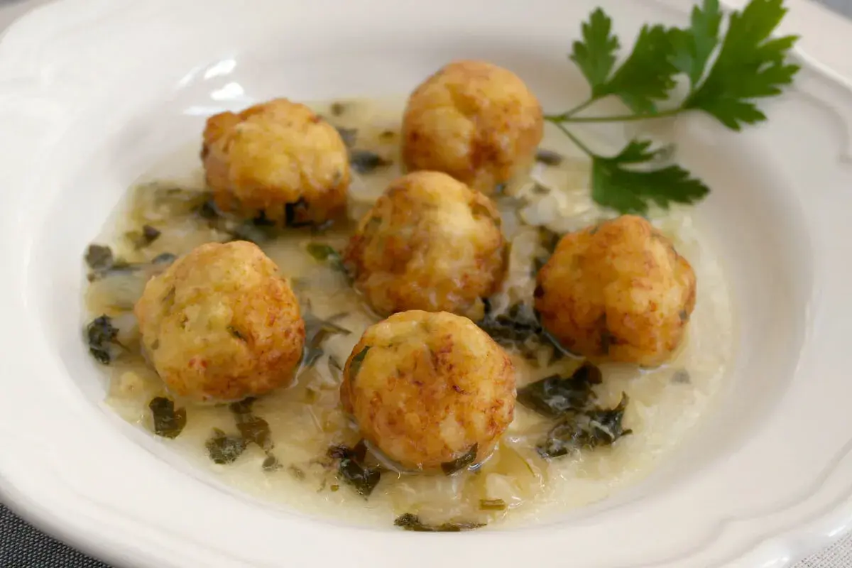 Seis albóndigas de merluza doradas flotan en una cremosa salsa verde con perejil fresco.