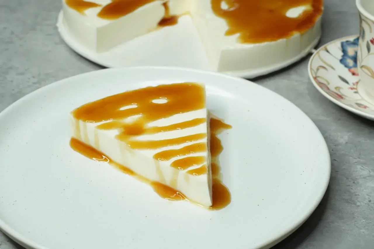 Una porción de tarta de cuajada, cremosa y blanca, bañada en un sirope dorado. El postre perfecto para un momento dulce.