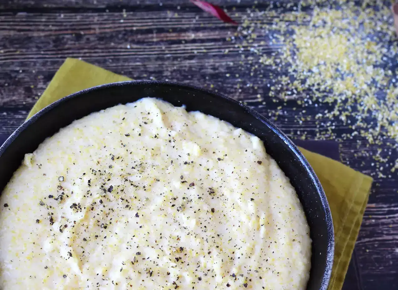 Cremosa polenta que es, servida en sartén negra, espolvoreada con pimienta negra.