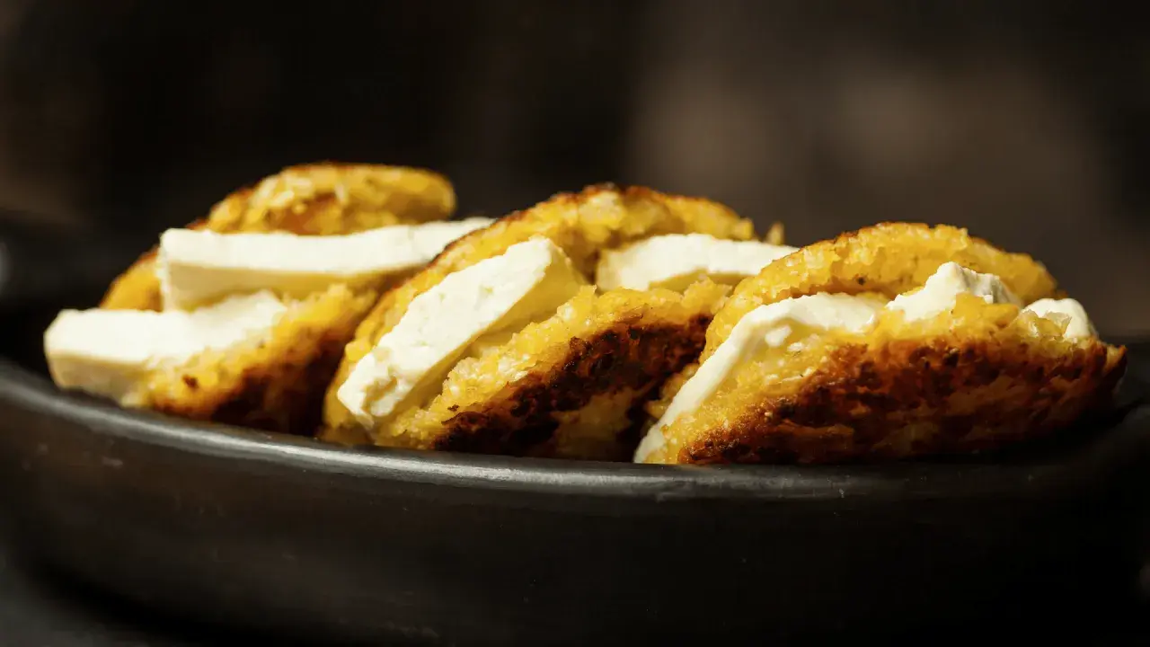 Arepas de choclo doradas y crujientes, rellenas de queso blanco fresco, servidas en un cuenco de barro.