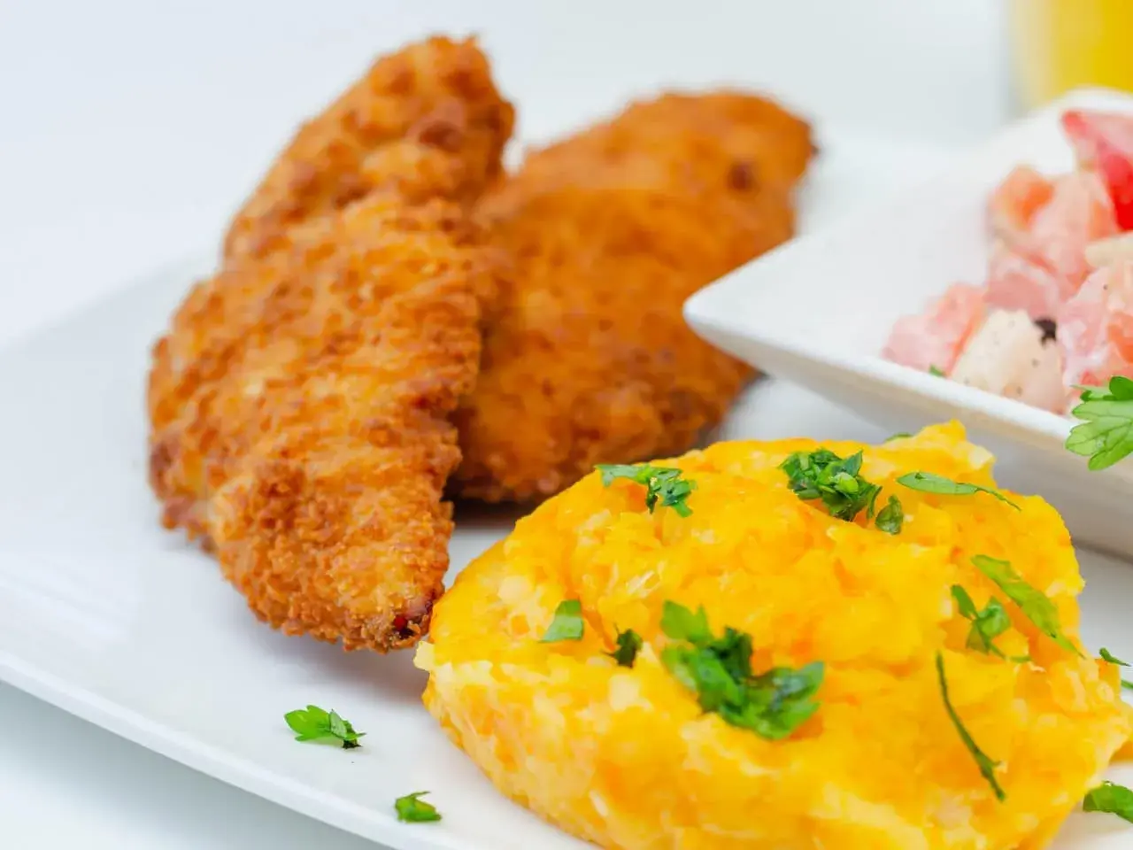 Crujiente solomillo de pollo empanado, puré de zanahoria y ensalada de tomate y cebolla.