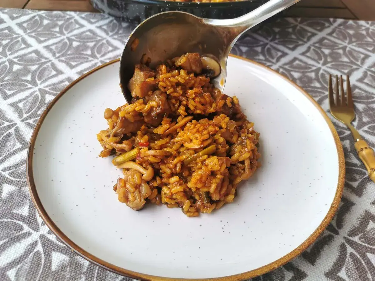 Un cucharón sirve arroz con secreto, un plato sabroso con carne y verduras, en un plato blanco.