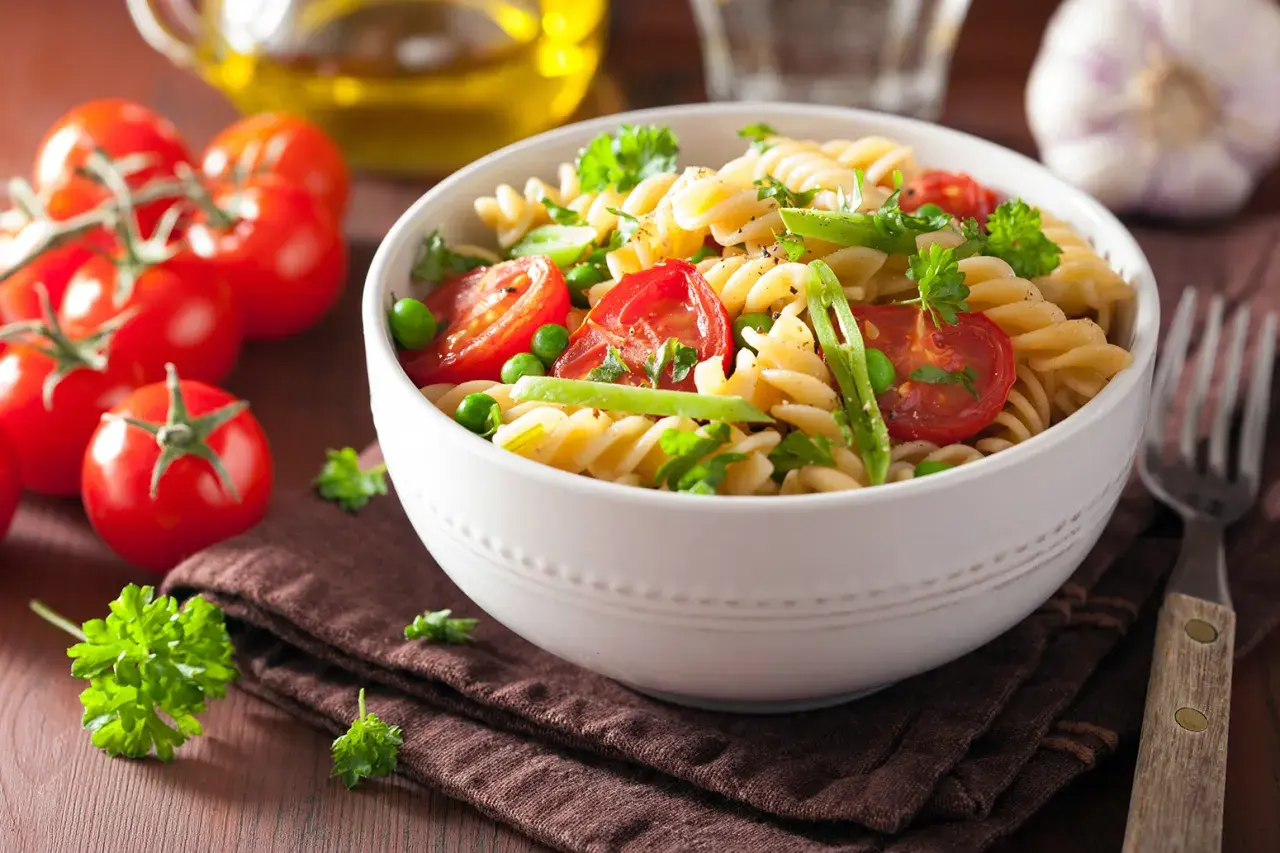 Un delicioso plato de pasta con verduras frescas, como tomates cherry, guisantes y perejil, servido en un cuenco blanco.