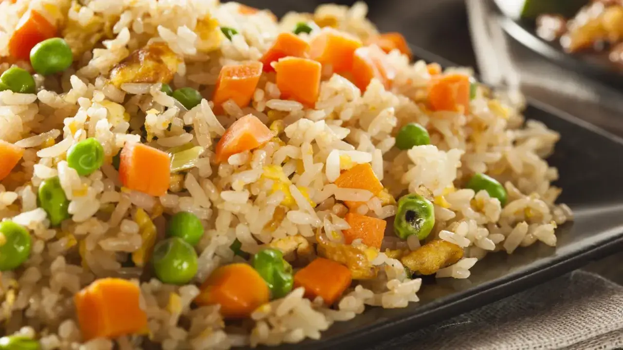 Arroz tres delicias con guisantes verdes, trozos de zanahoria y huevo revuelto, servido en un plato negro.