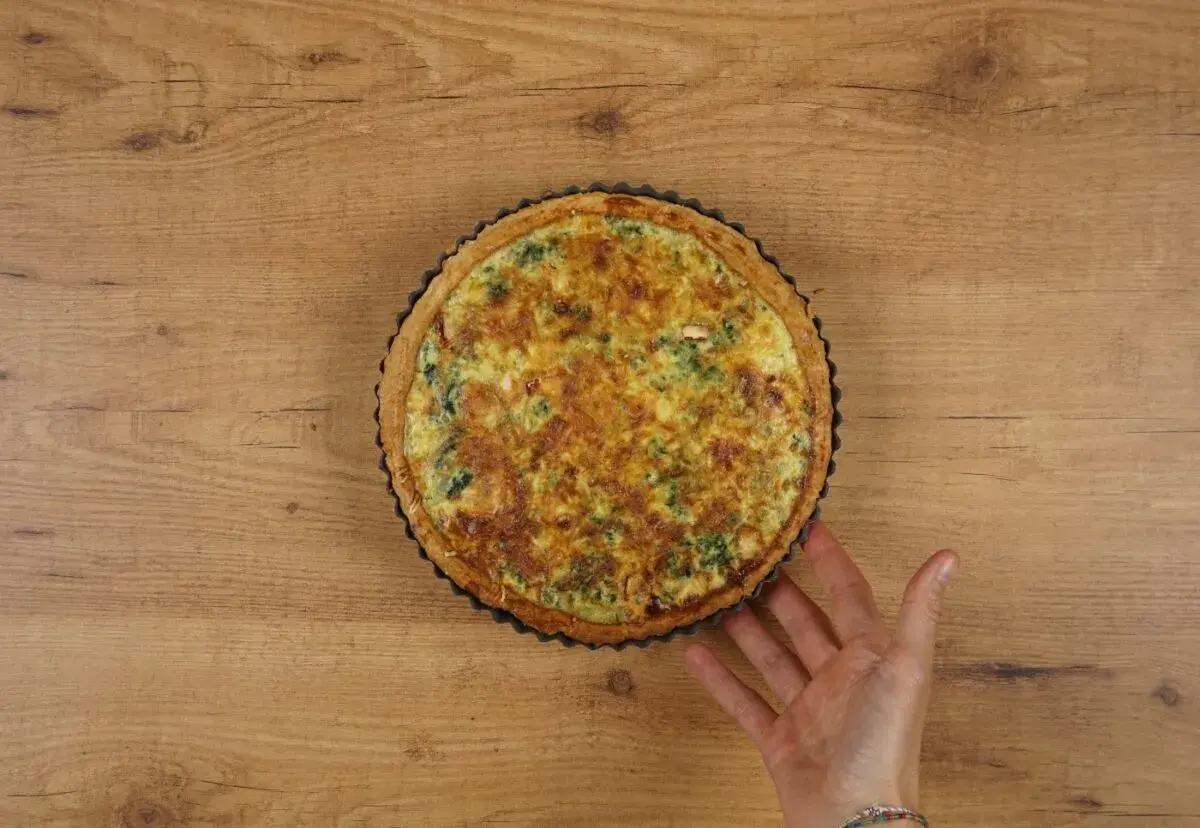 Un delicioso quiche de espinacas recién horneado, con una mano que lo sujeta suavemente.