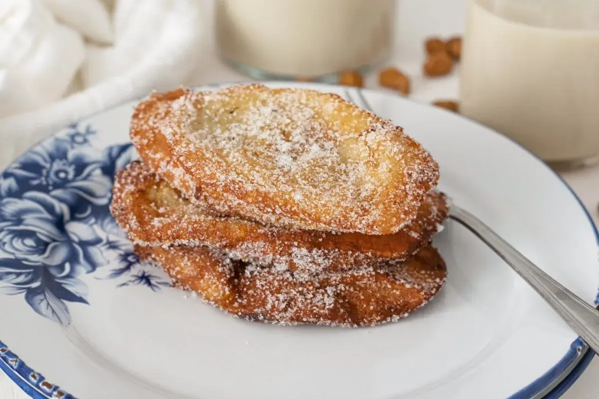 Tres torrijas de horchata, doradas y espolvoreadas con azúcar, apiladas en un plato con diseño floral azul.