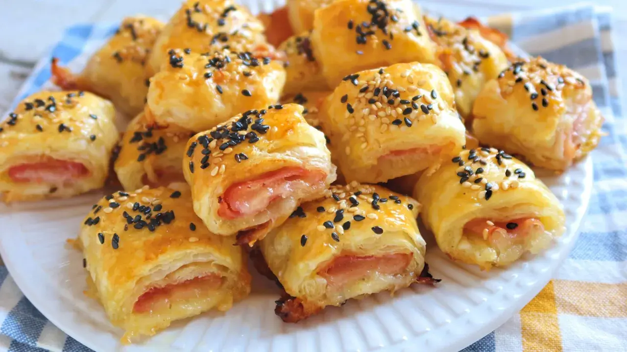 Rollitos de hojaldre jamón y queso, dorados y espolvoreados con semillas de sésamo negro y blanco.