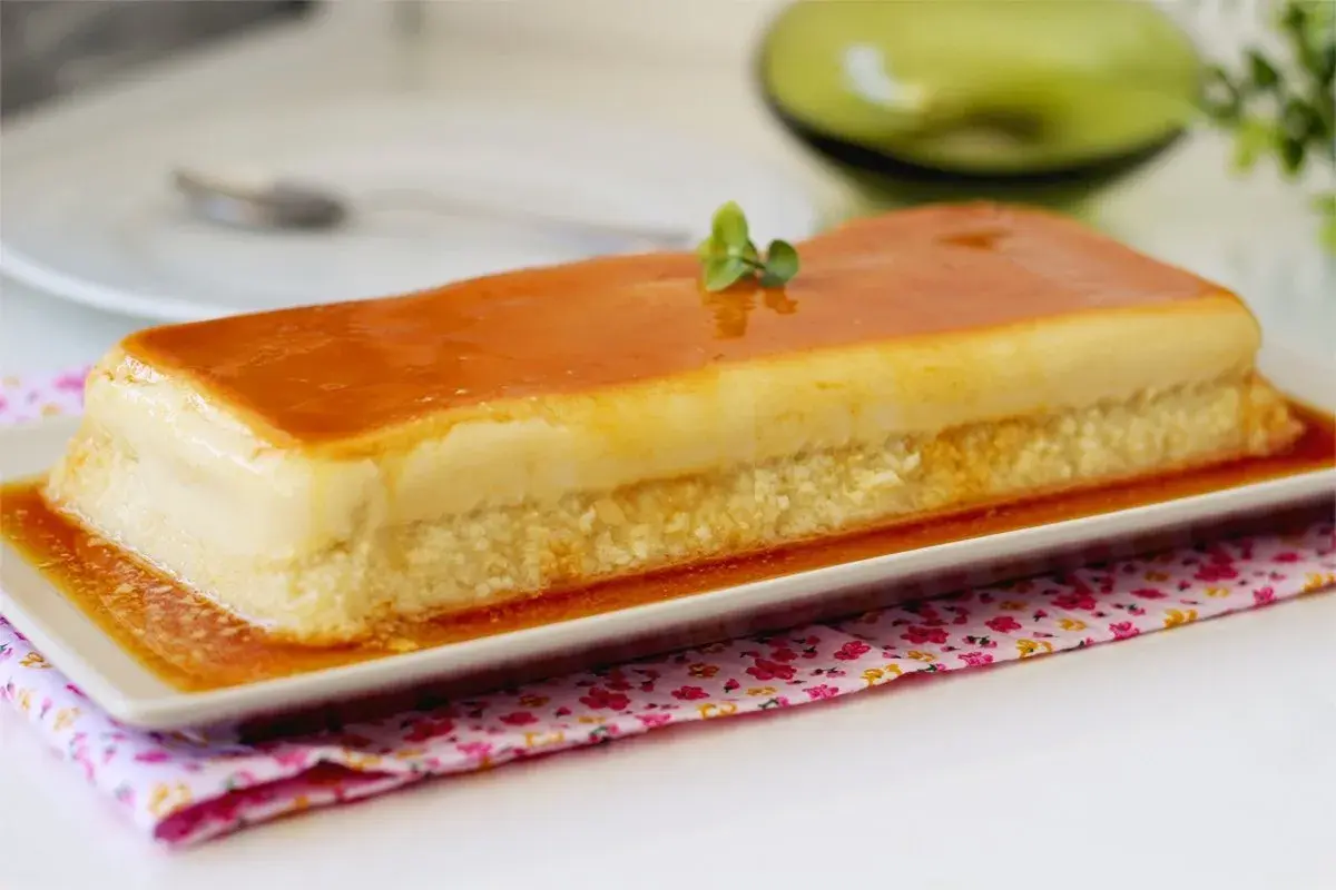 Un delicioso flan de manzana rectangular, cubierto de caramelo dorado y decorado con una ramita verde.