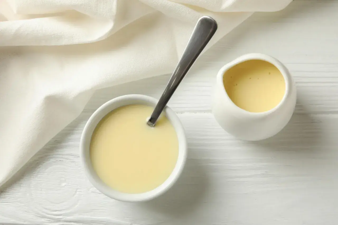 Leche evaporada en un tazón con cuchara y jarra, lista para usar en recetas.