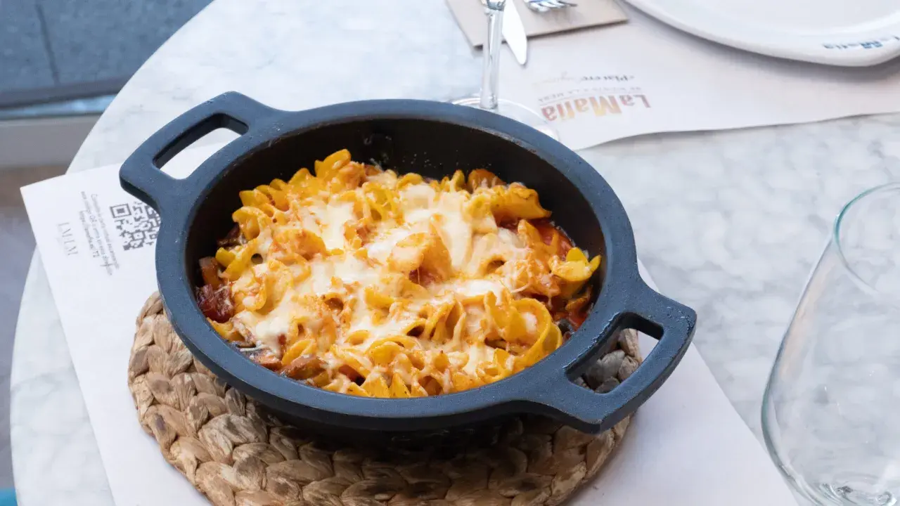 Macarrones al horno gratinados con queso fundido, servidos en una cazuela negra sobre un mantel de mármol.