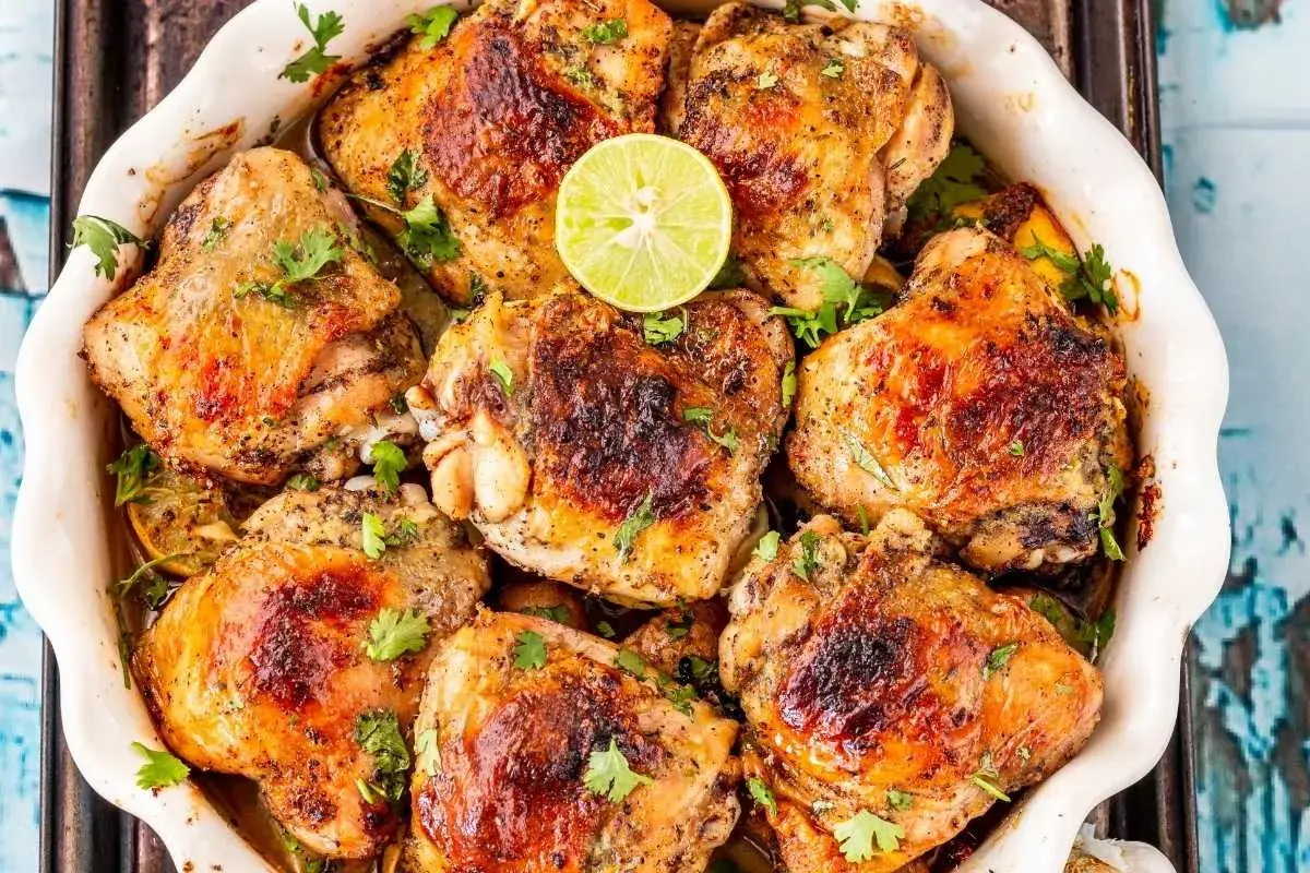 Muslos de pollo dorados y jugosos, horneados con limón y hierbas frescas, listos para servir.