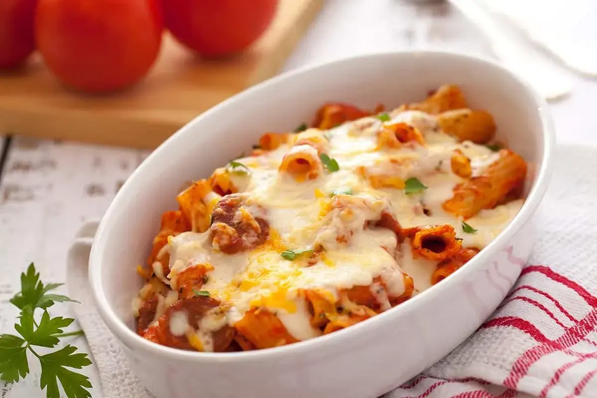 Macarrones con chorizo gratinados, cubiertos de queso derretido y perejil fresco, servidos en una fuente blanca.
