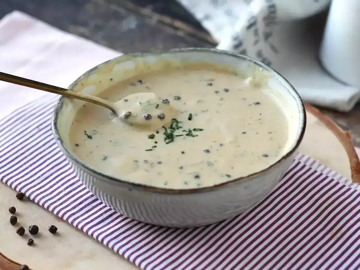 Un cuenco de cremosa salsa a la pimienta, con un toque de perejil picado y granos de pimienta negra esparcidos.