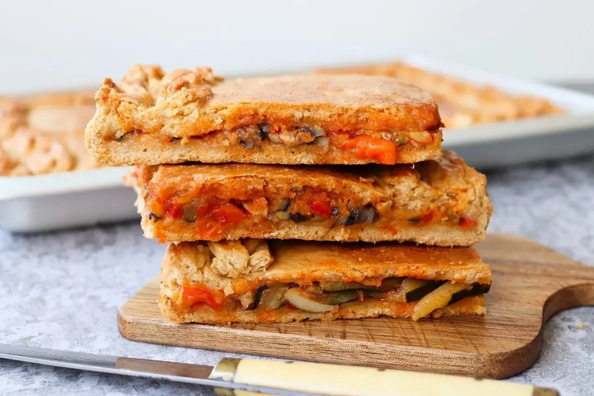 Tres porciones de empanada de verduras apiladas, mostrando el relleno de pimientos, calabacín y tomate.