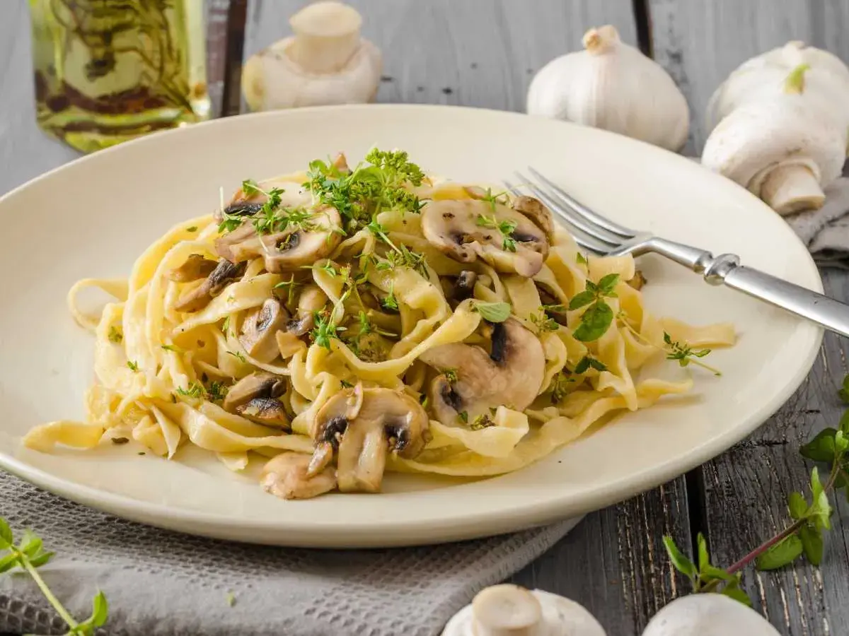 Deliciosa pasta con champiñones frescos y hierbas aromáticas, servida en un plato cremoso.