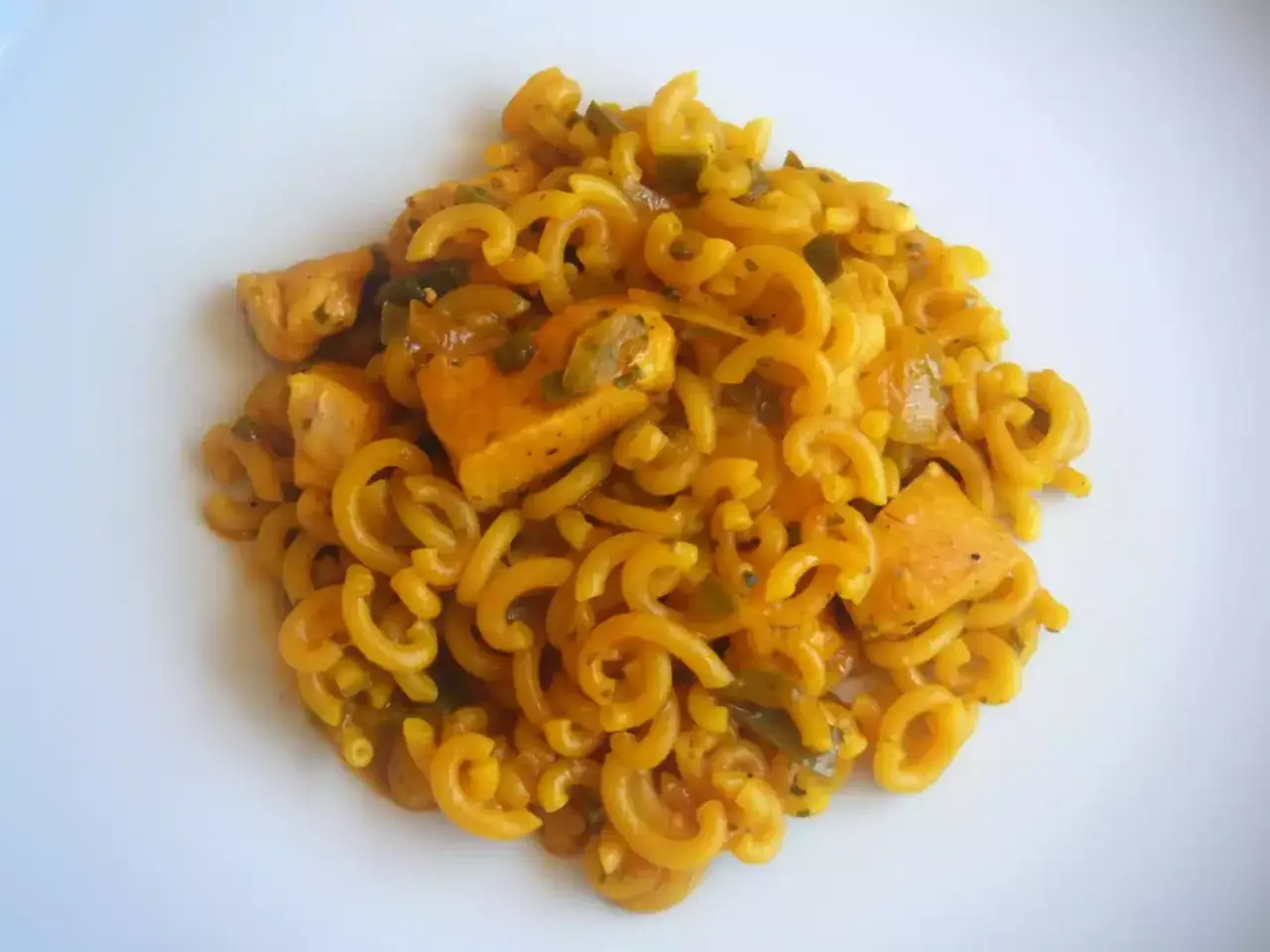 Fideuà de pollo con fideos rizados y trozos de pollo en salsa dorada, servida en plato blanco.