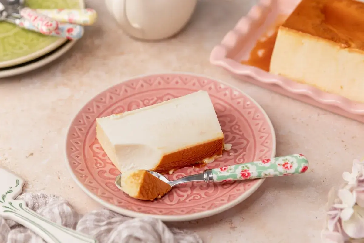 Un trozo de flan de queso cremoso con caramelo dorado, servido en un plato rosa.